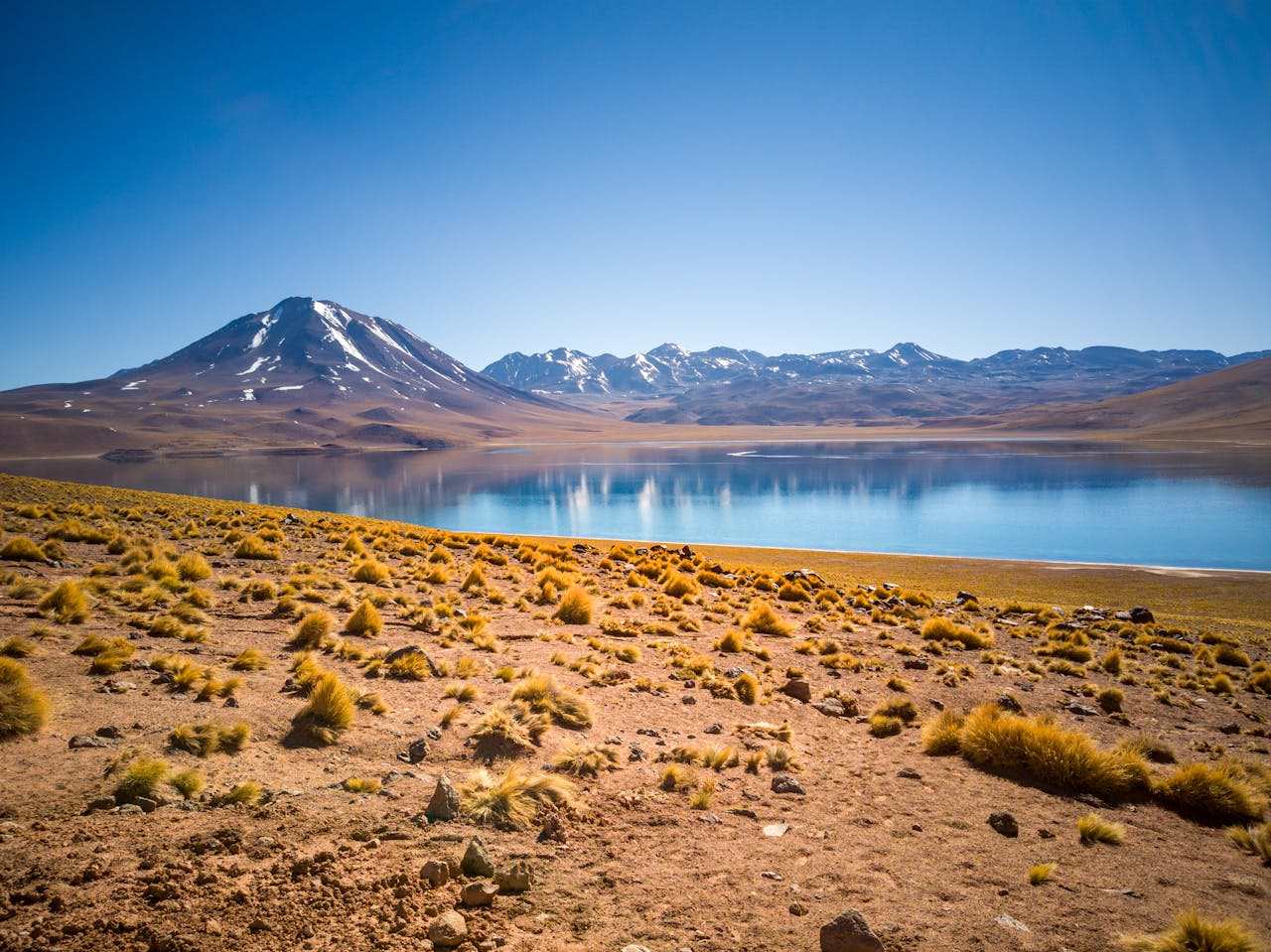 Dramatic landscape of the Atacama Desert featuring a mountain and lagoon under a clear sky.